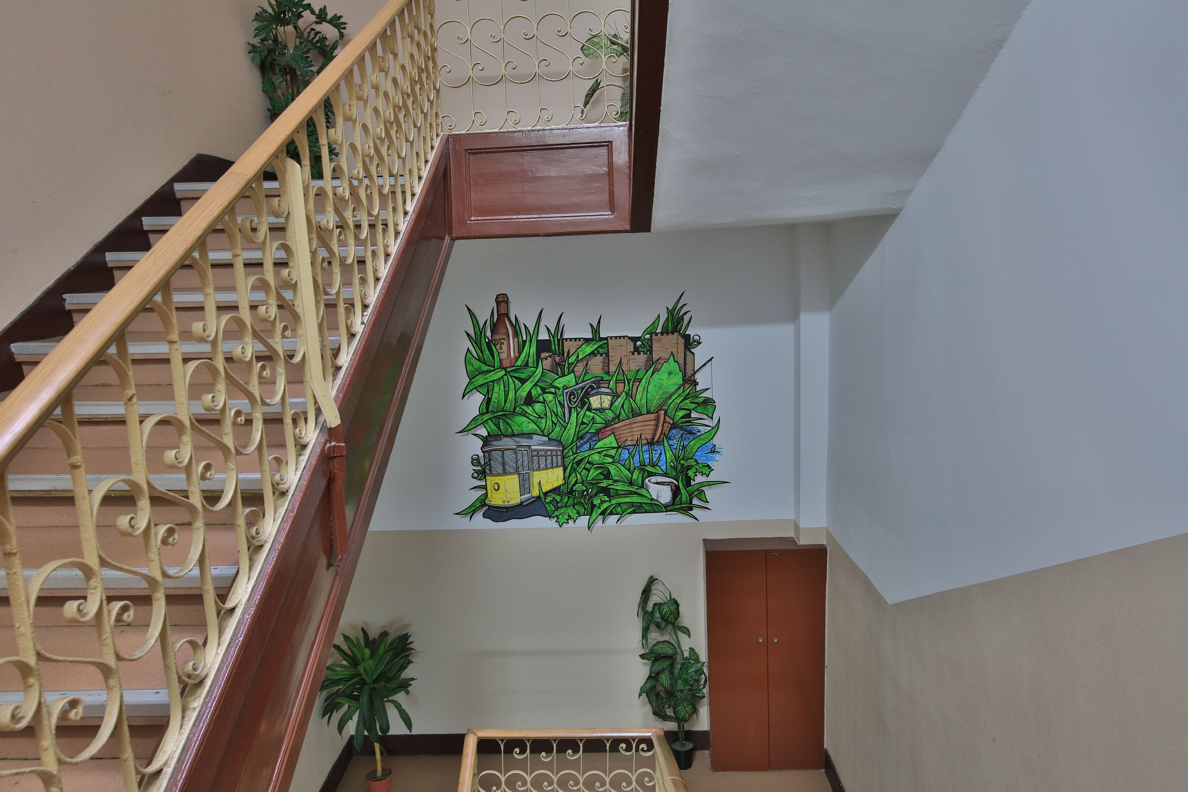 Een trap met een decoratieve balustrade, een muurschildering met groene begroeiing en een oldtimer, en een houten deur onderaan.
