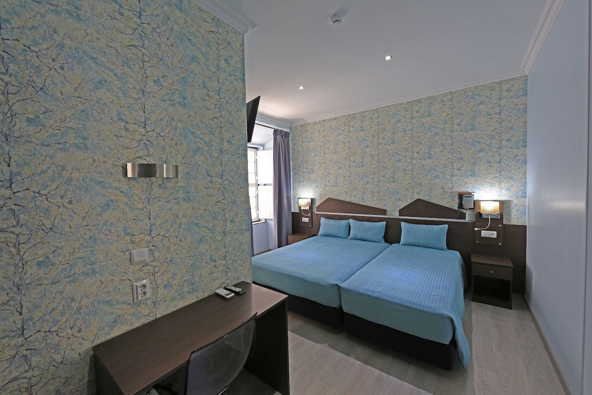 Een hotelkamer met een groot bed, een bureau en een nachtkastje met een lamp.