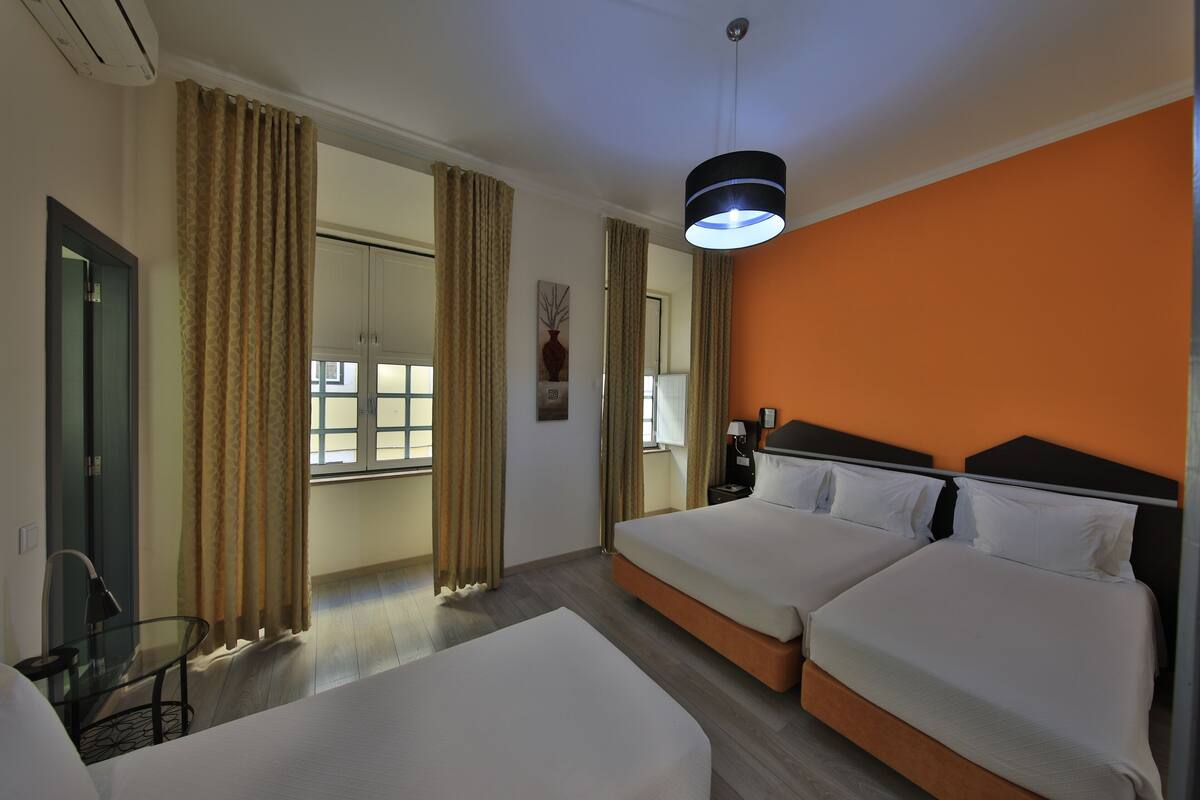 Een hotelkamer met twee bedden, een groot raam met gordijnen, een nachtkastje en een hanglamp.