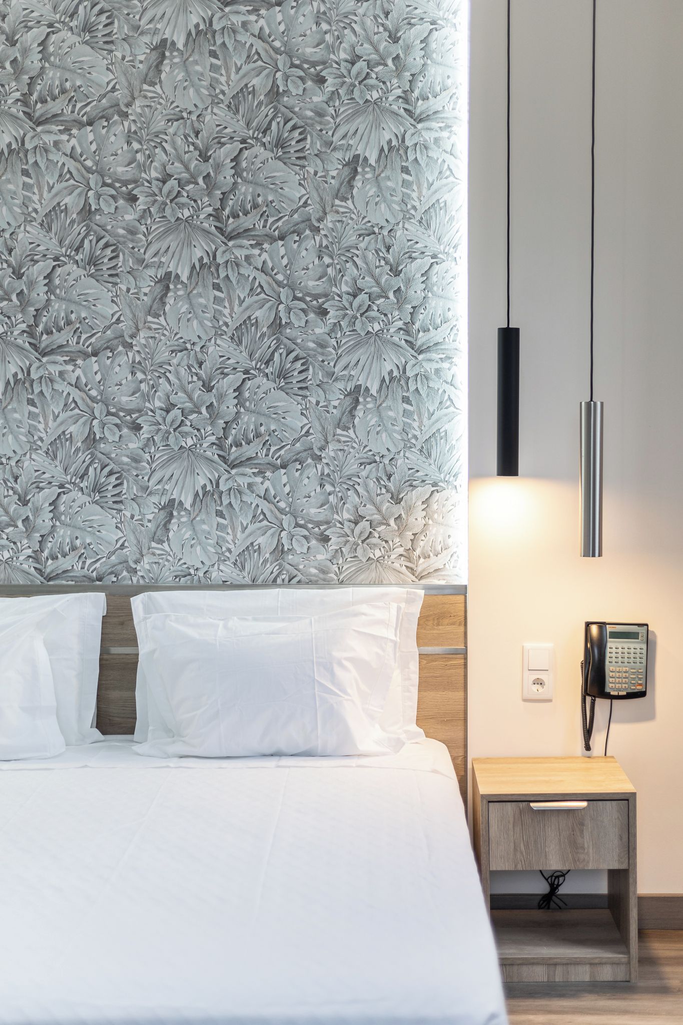Ein Hotelzimmer mit einem Bett, einem Nachttisch mit Telefon und einer Wand mit Blättermuster.