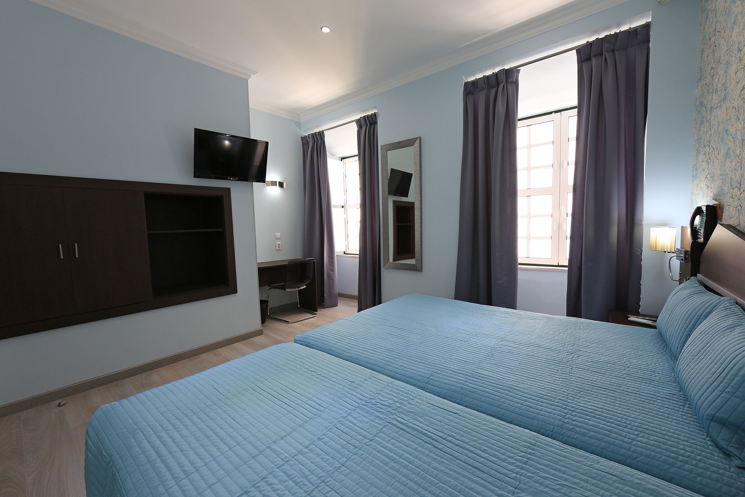 A hotel room with two beds, a TV, a desk, and a mirror.