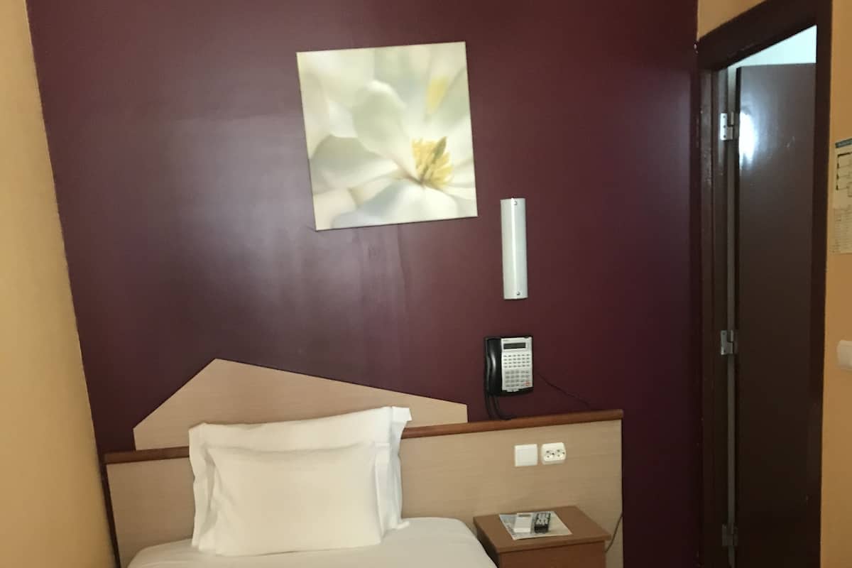 Een hotelkamer met een bed, nachtkastje, telefoon en deur.