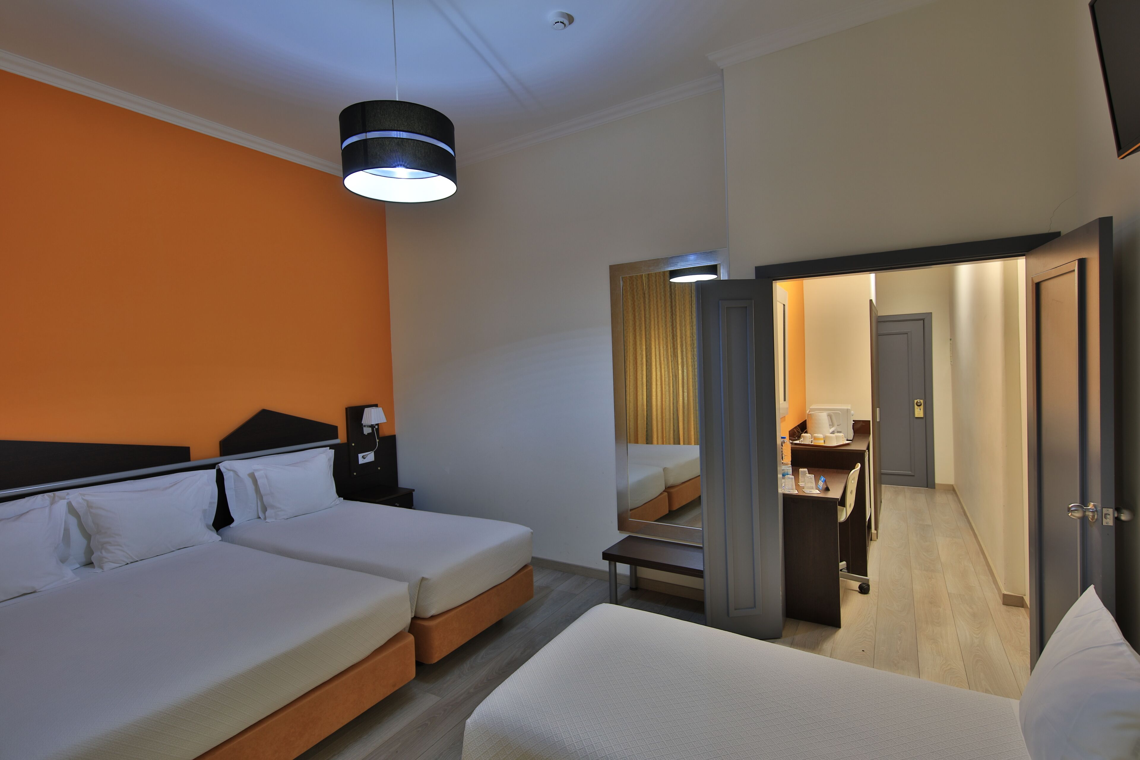A hotel room with two beds, a desk, and a mirror.
