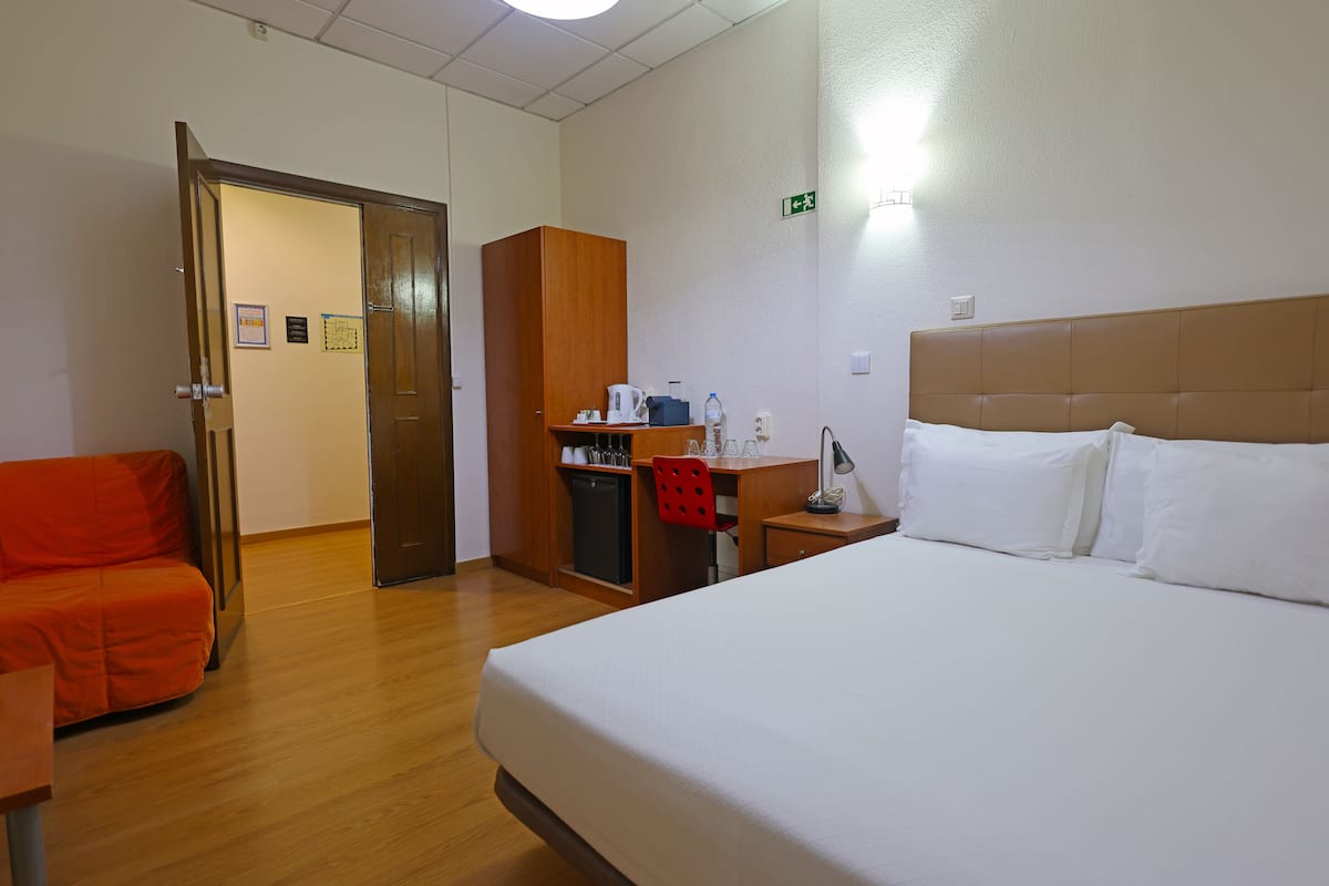 Een hotelkamer met een bed, een bureau met stoel, een kledingkast en een klein keukenhoekje.