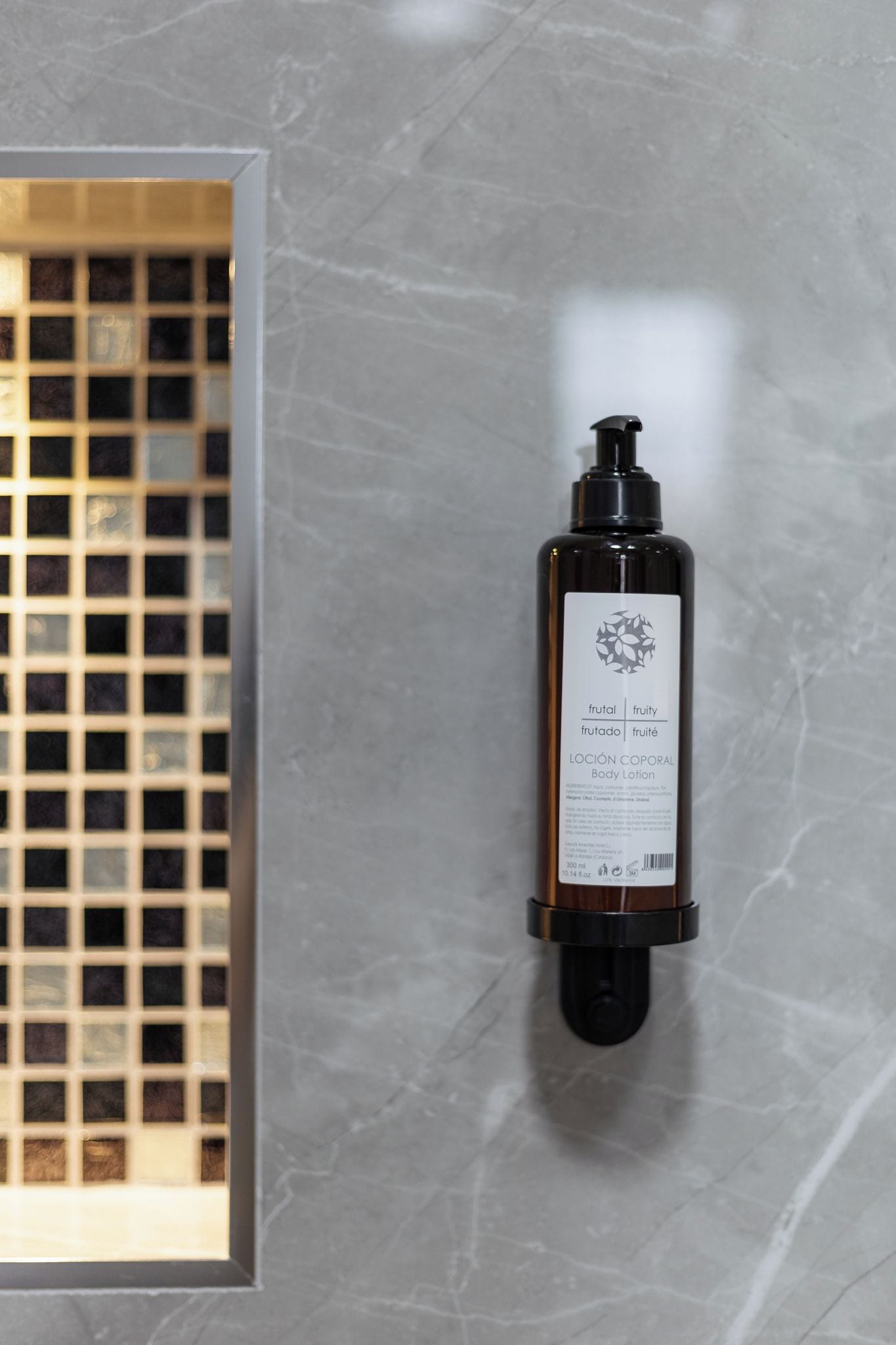 A bottle of body lotion with a label, mounted on a wall with a grid-like window.