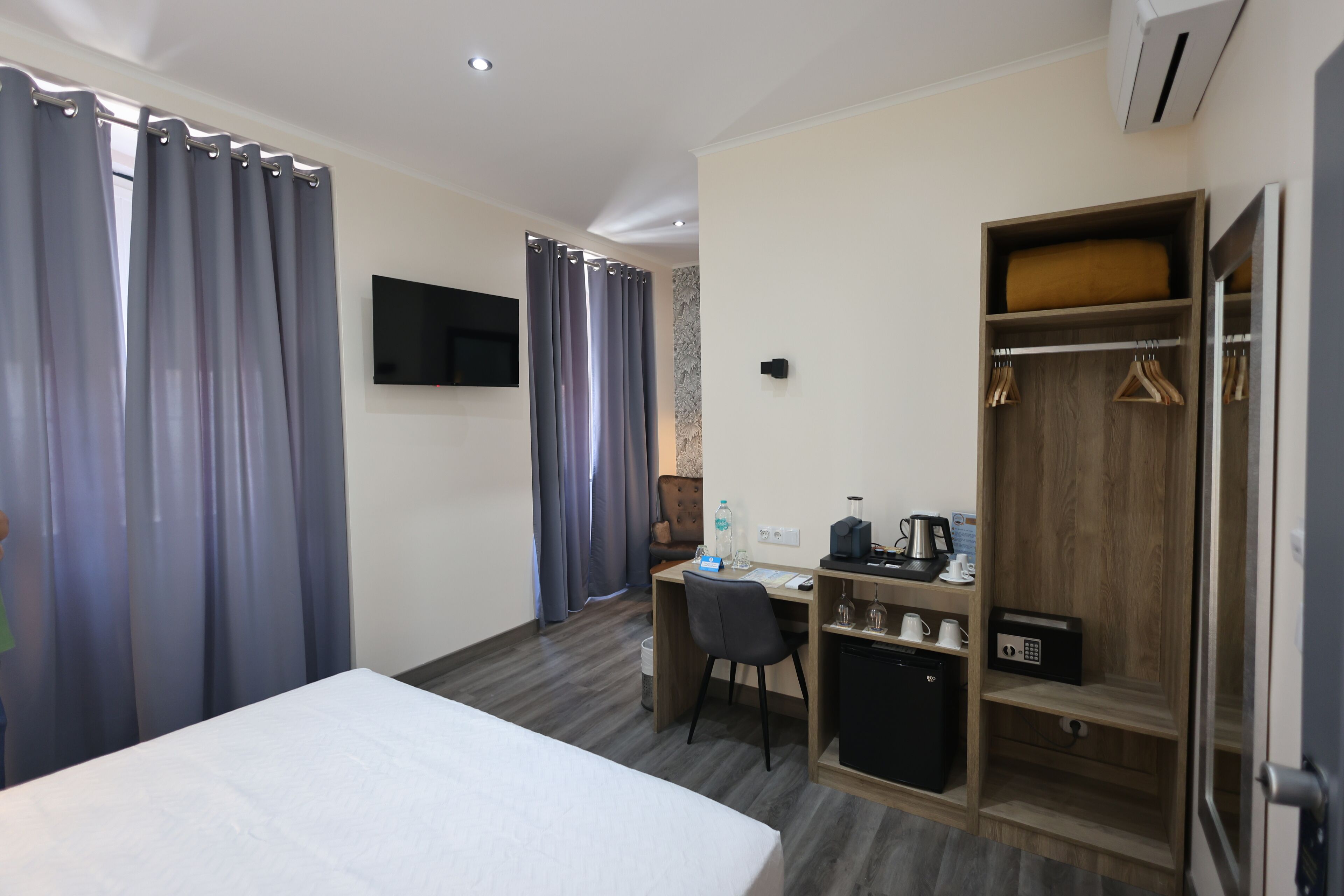 Una habitación de hotel con cama, escritorio con silla, armario y televisor en la pared.