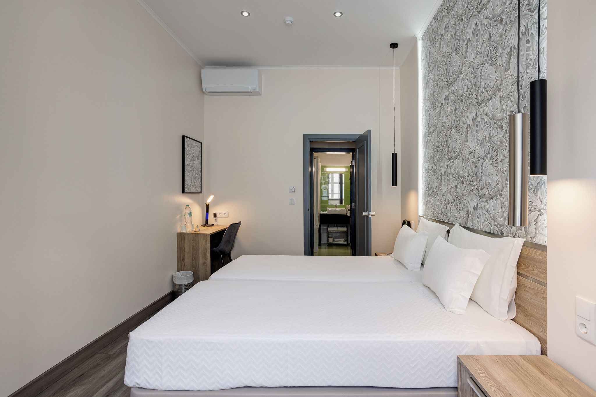 Habitación de hotel con una cama grande, una mesita de noche, una lámpara de pared y una puerta que da al baño.