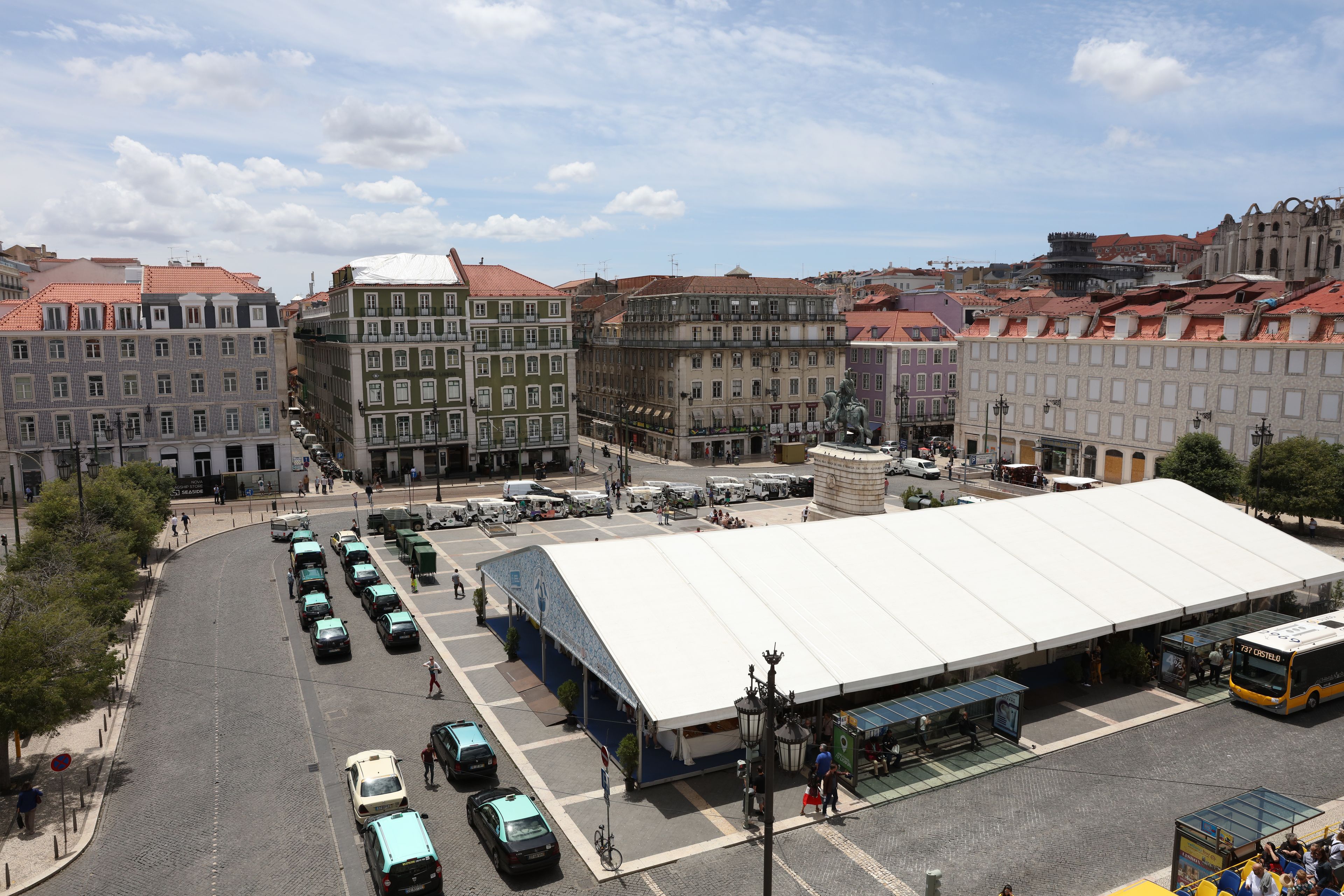 Ein Stadtplatz mit einem großen weißen Zelt, geparkten Autos und historischen Gebäuden.