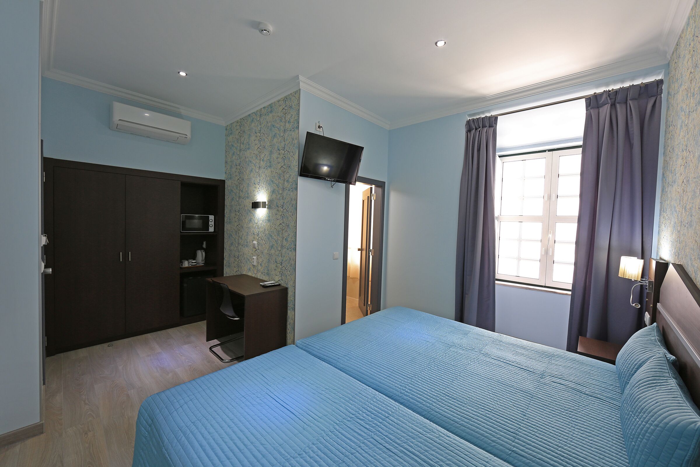 Slaapkamer met een groot bed, een kledingkast, een bureau, een flatscreen televisie en een raam met gordijnen.