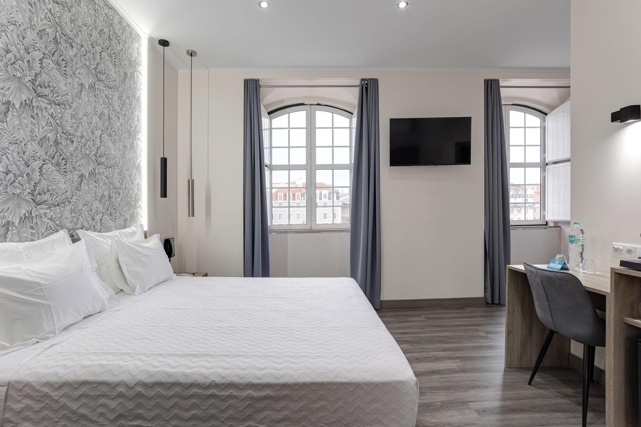 Habitación de hotel con una cama grande, un escritorio, un televisor de pantalla plana y un ventanal con cortinas.