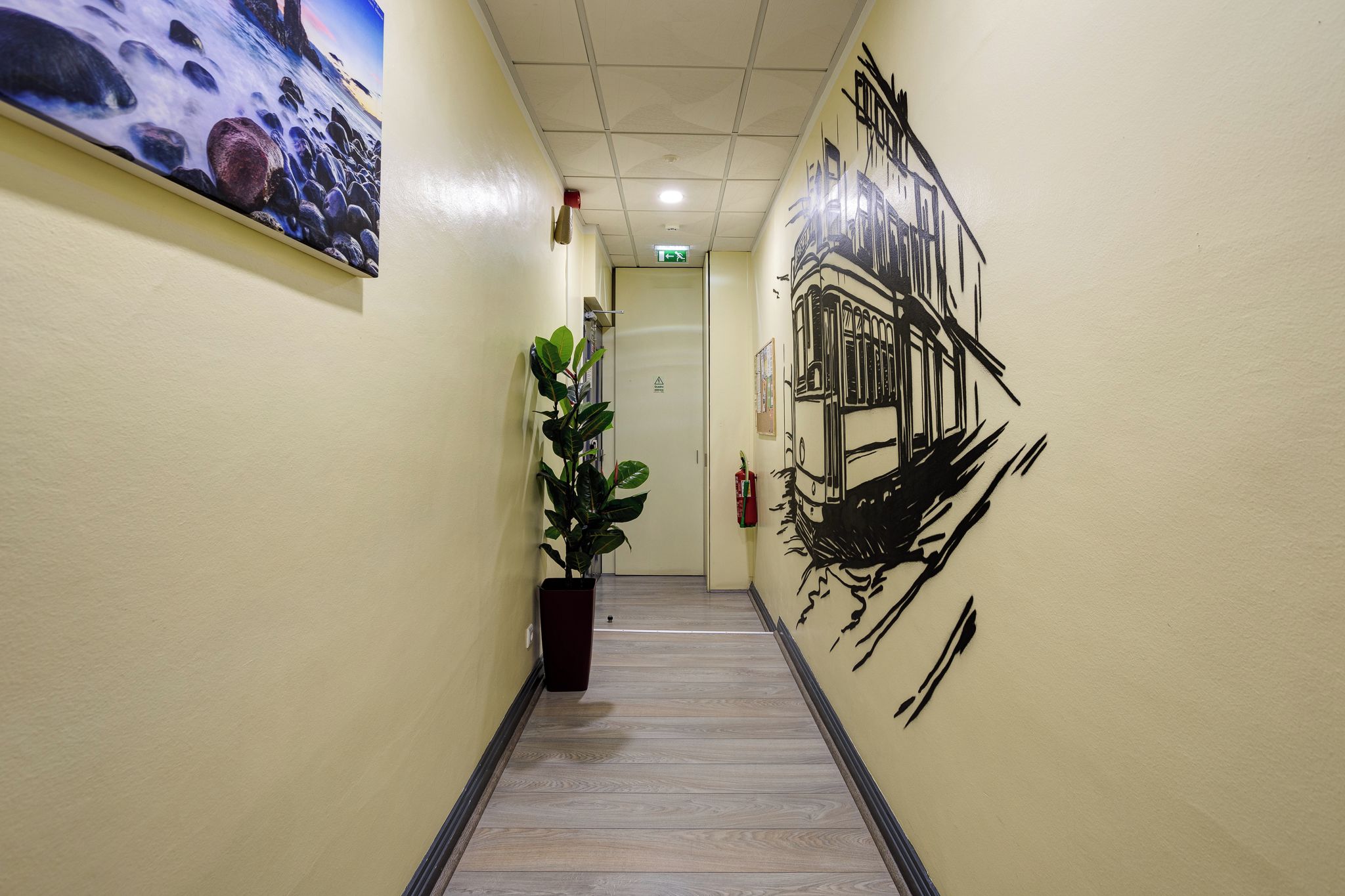 Un pasillo con piso de madera, una planta en maceta y un mural de un tranvía en la pared.