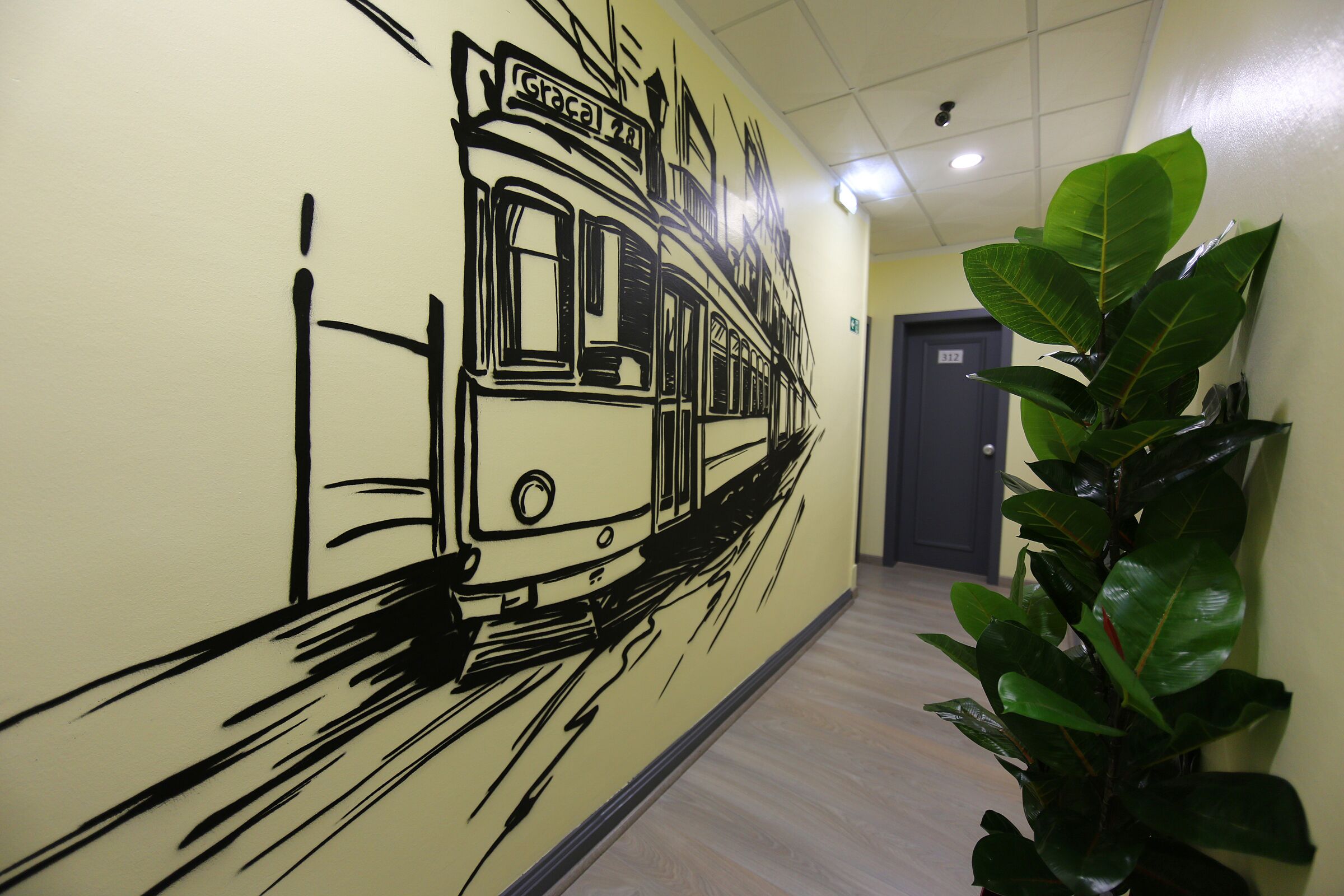 A hallway with a mural of a tram, a potted plant, and a door in the background.