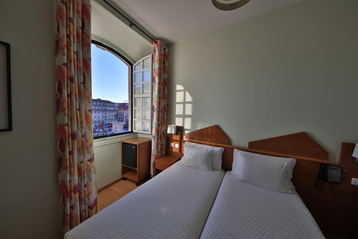 Hotelkamer met een groot bed, een bureau, een stoel, een klein kastje en een raam met gordijnen.