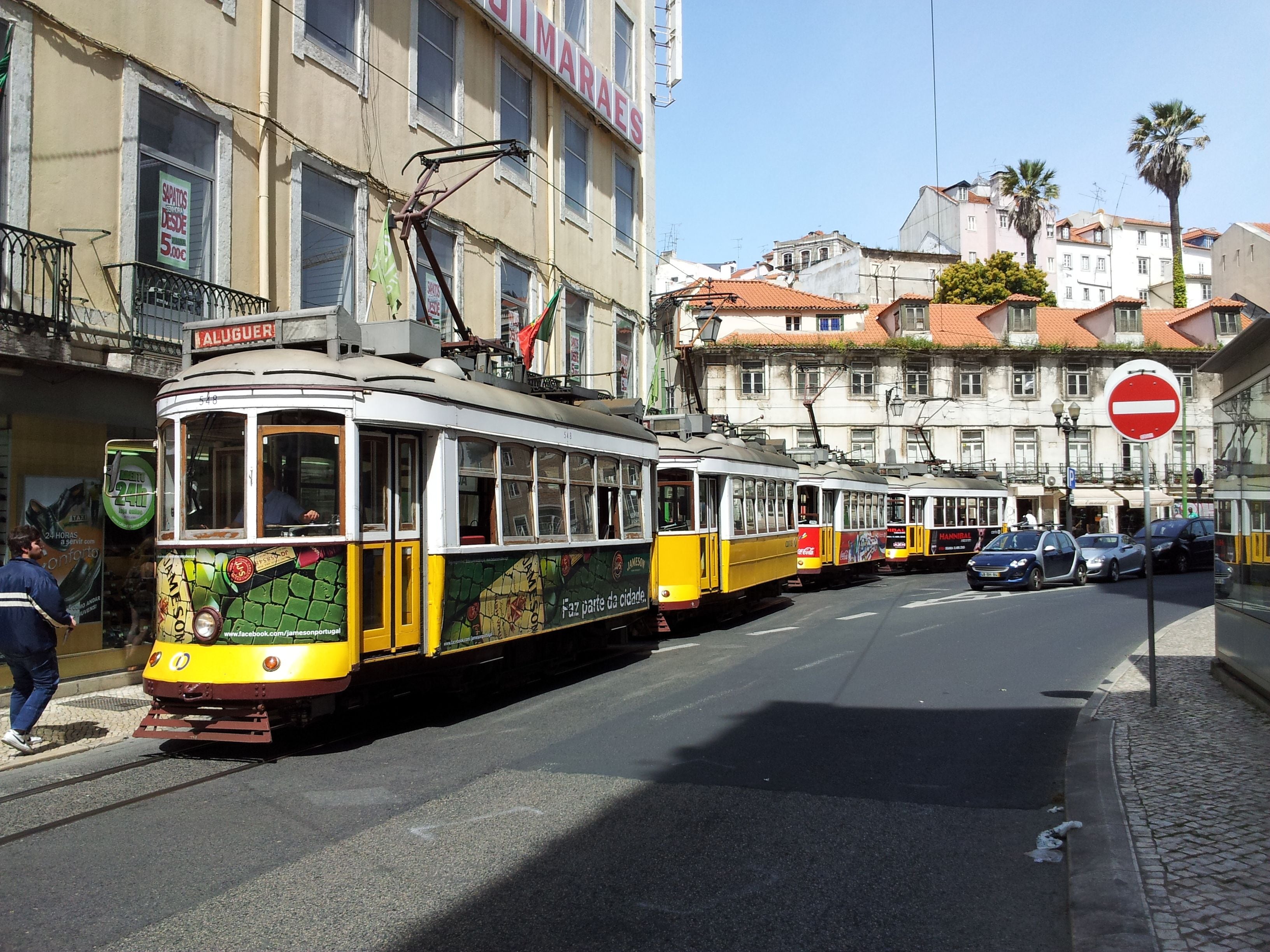 Eine Straßenbahn mit grün-gelbem Design, geparkt in einer Straße mit Gebäuden und blauem Himmel im Hintergrund.