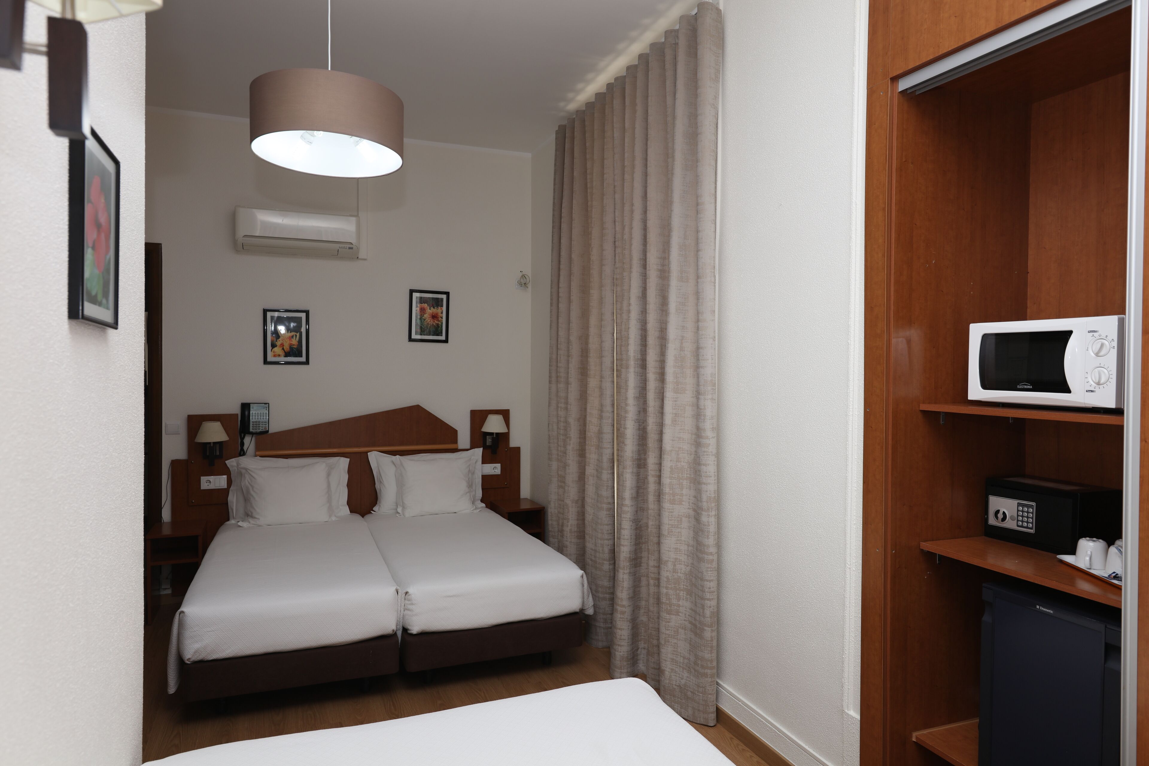Hotellihuone, jossa on parivuode, puinen pääty, yöpöytä lampulla, vaatekaappi ja mikroaaltouuni.