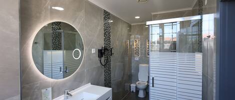 Un baño moderno con un espejo grande, un lavamanos blanco y una zona de ducha con mampara de cristal.