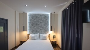 Een moderne hotelkamer met een groot bed, twee nachtkastjes, een telefoon aan de muur en een gordijn aan de rechterkant.