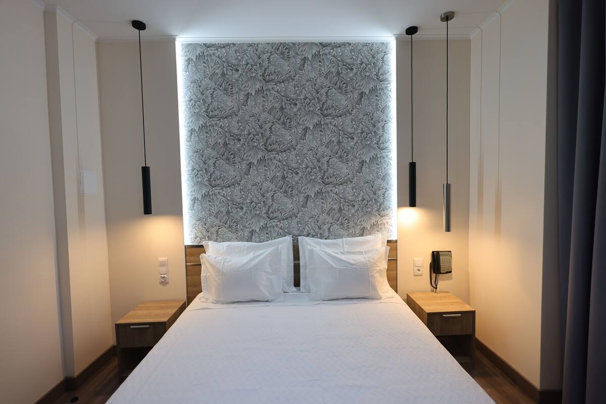 Een moderne slaapkamer met een groot bed, twee nachtkastjes, een telefoon aan de muur en een decoratief hoofdeinde.