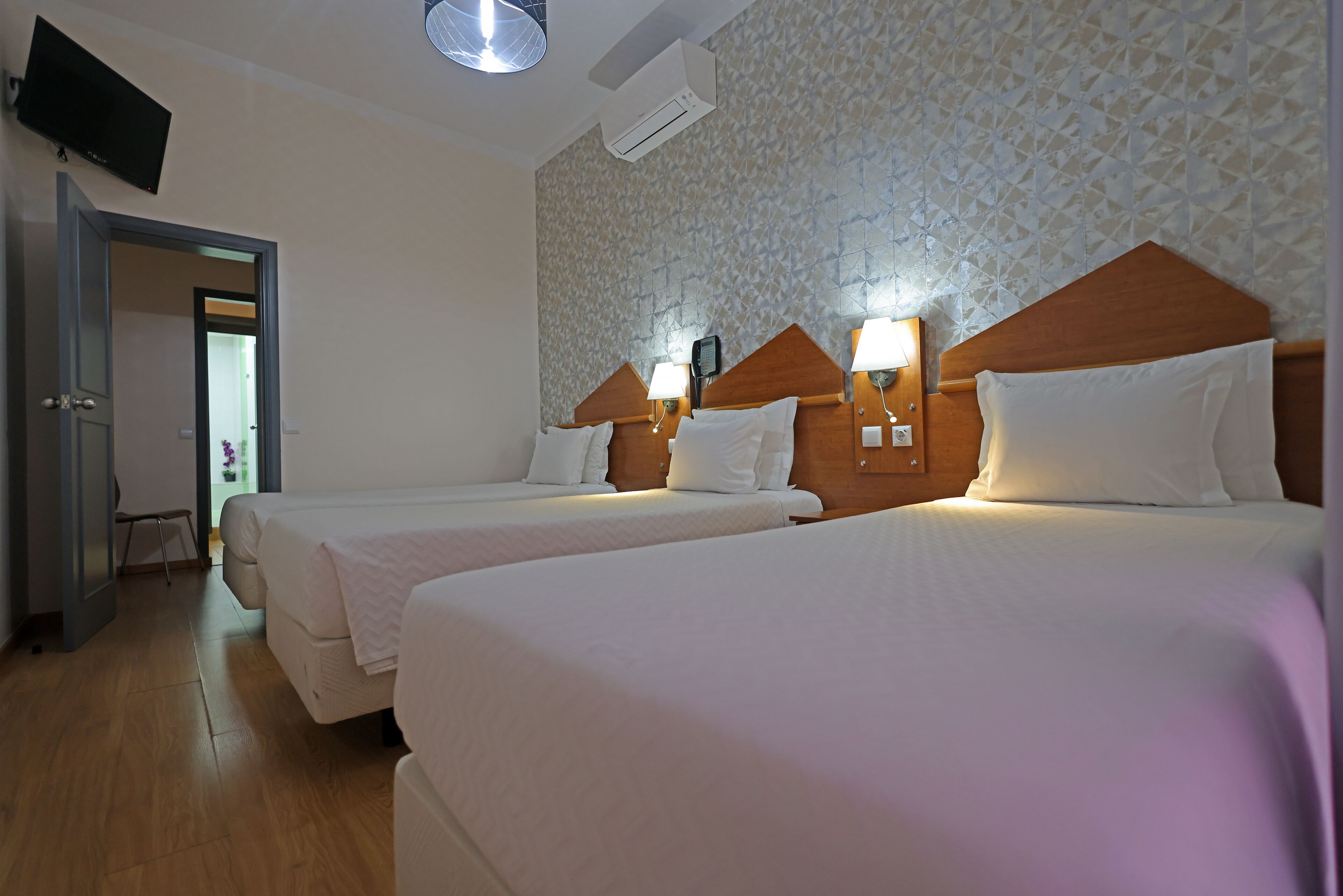 Ett hotellrum med två sängar, en tv, en luftkonditioneringsanläggning och en vägg med ett mönster.