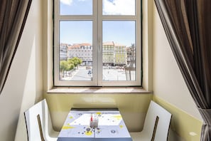 A room with a table and chairs, a window with a view of buildings, and a curtain.