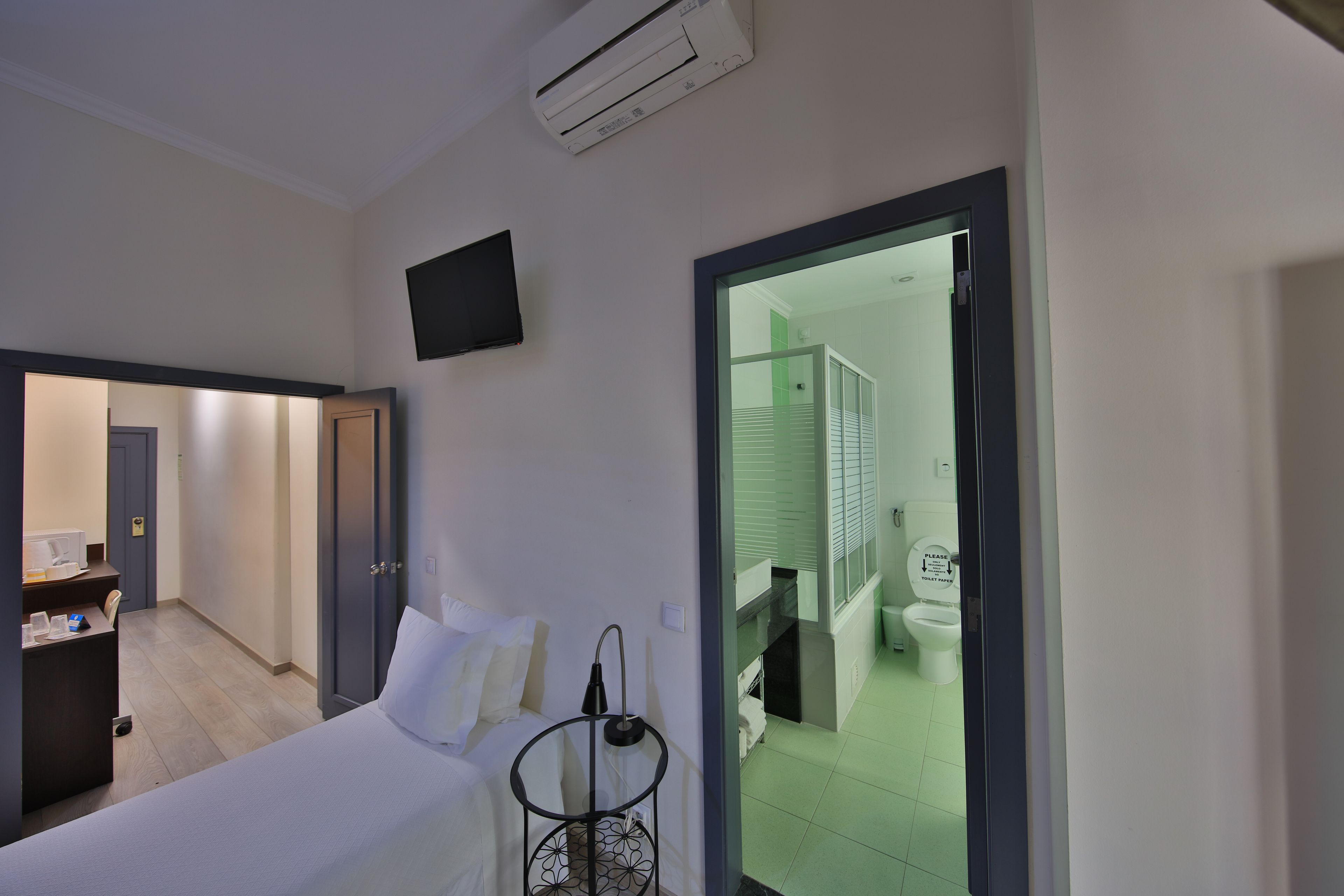 Une chambre d’hôtel comprenant un lit, une table de chevet, un téléviseur fixé au mur et une porte donnant accès à la salle de bain.
