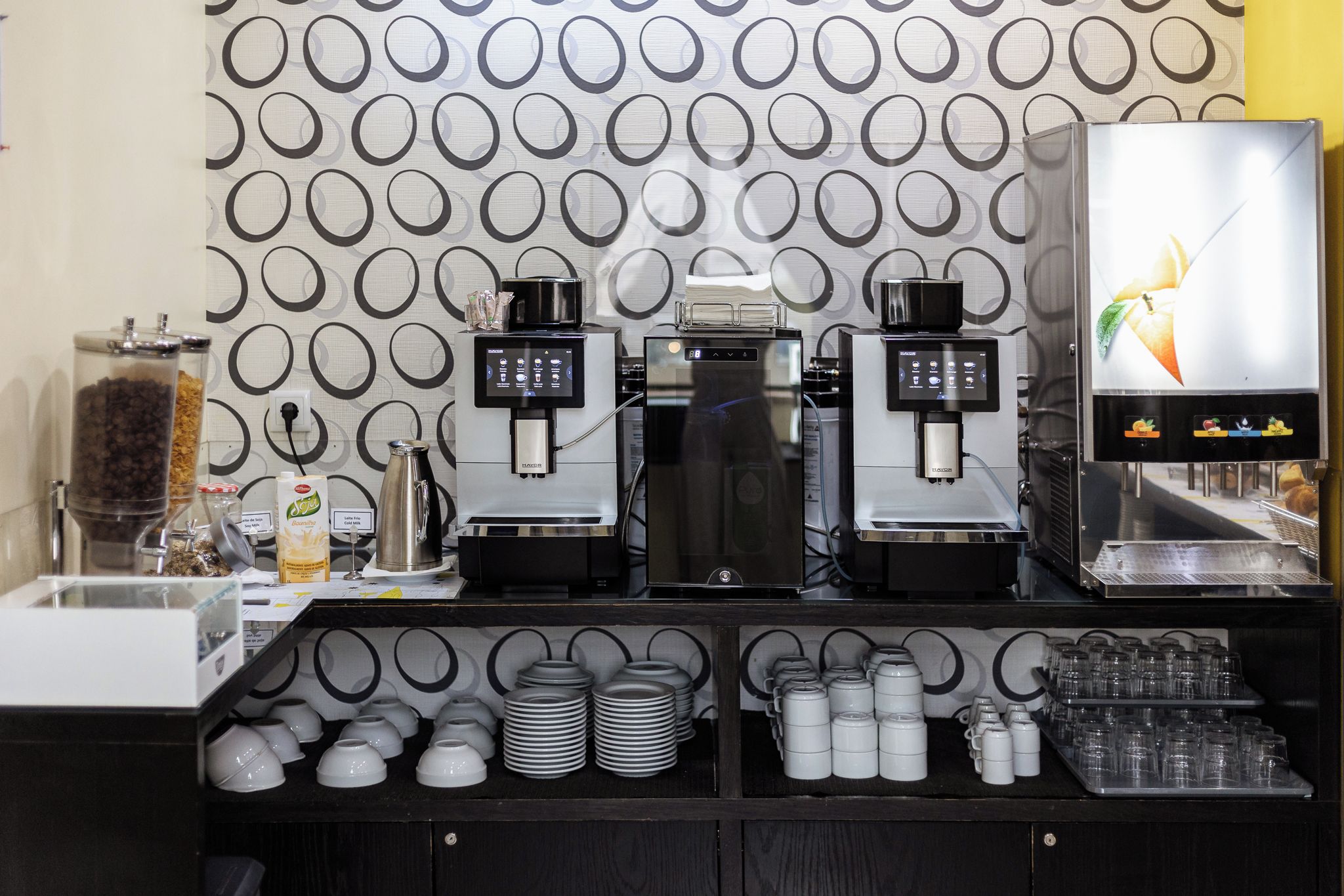 A coffee station with two espresso machines, a milk frother, and a variety of coffee cups and saucers.