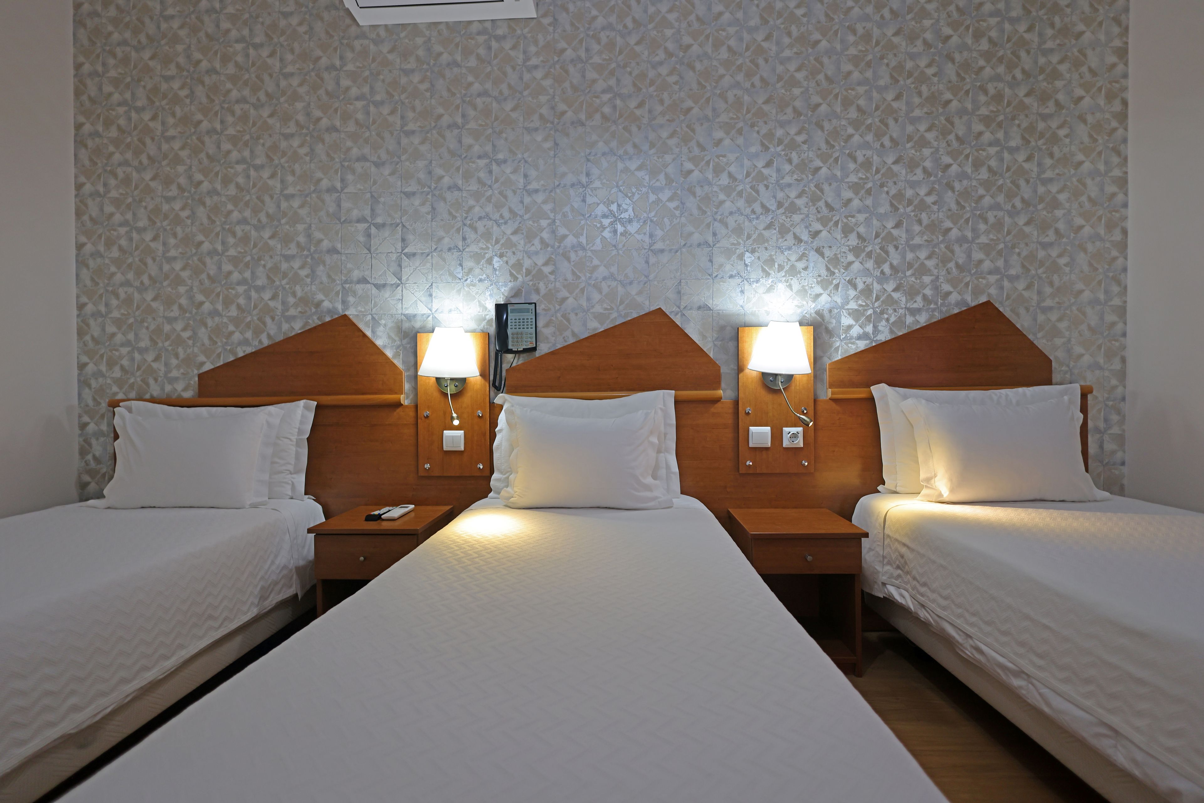 Habitación de hotel con dos camas individuales, cada una con cabecero de madera, mesitas de noche y lámparas de pared.