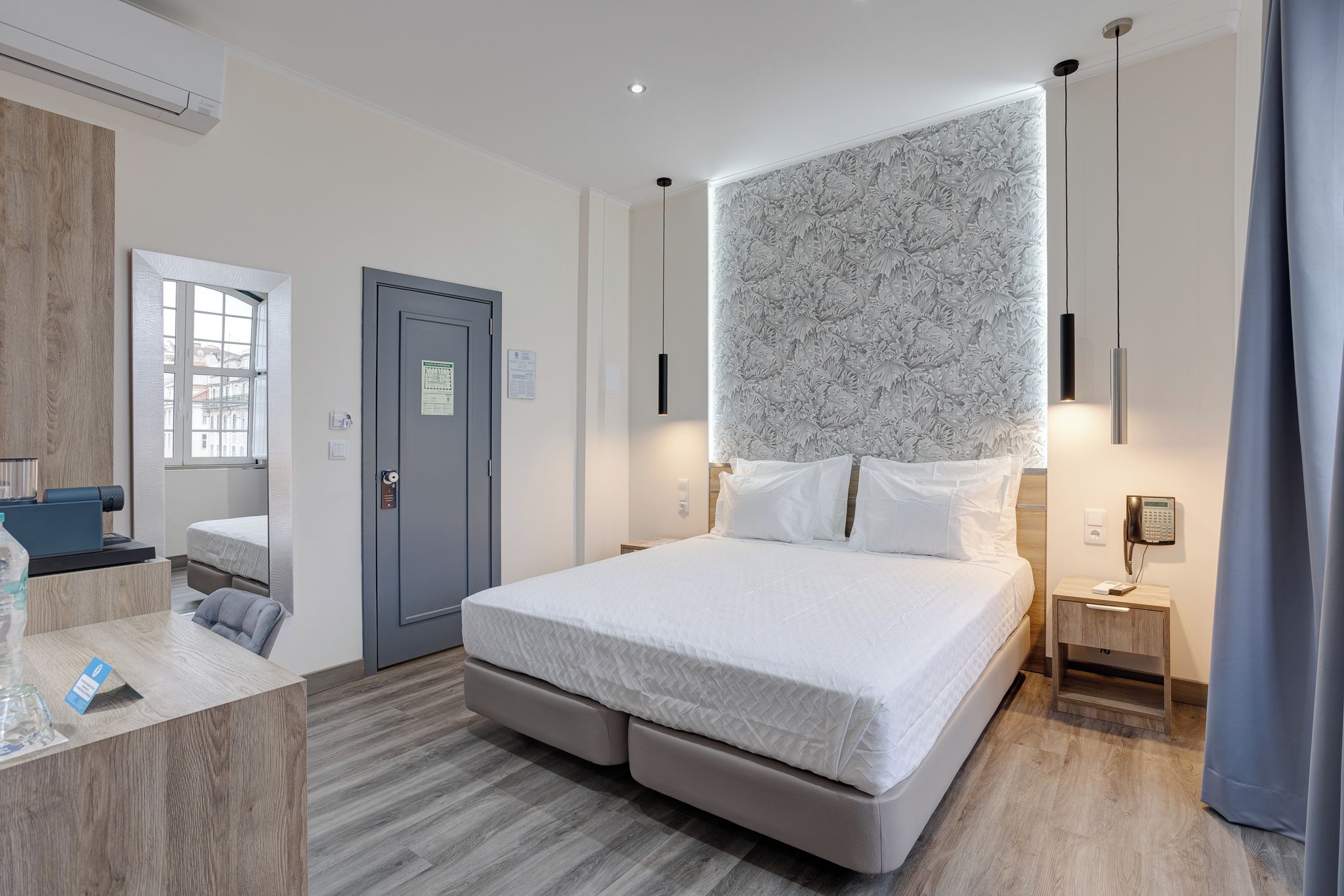 Una habitación de hotel con cama, escritorio, silla, armario, puerta y ventana.