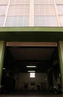 Entrada de um edifício com moldura verde, porta de garagem e uma pequena janela no alto.