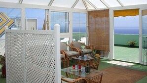 A covered outdoor area with a glass table and wicker chairs, overlooking a green landscape and the sea. - Apartamentos Mayoysa (Brena Baja)
