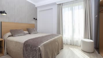 A modern bedroom with a large bed, bedside lamps, a wooden headboard, a bedside table, and a large window with curtains.