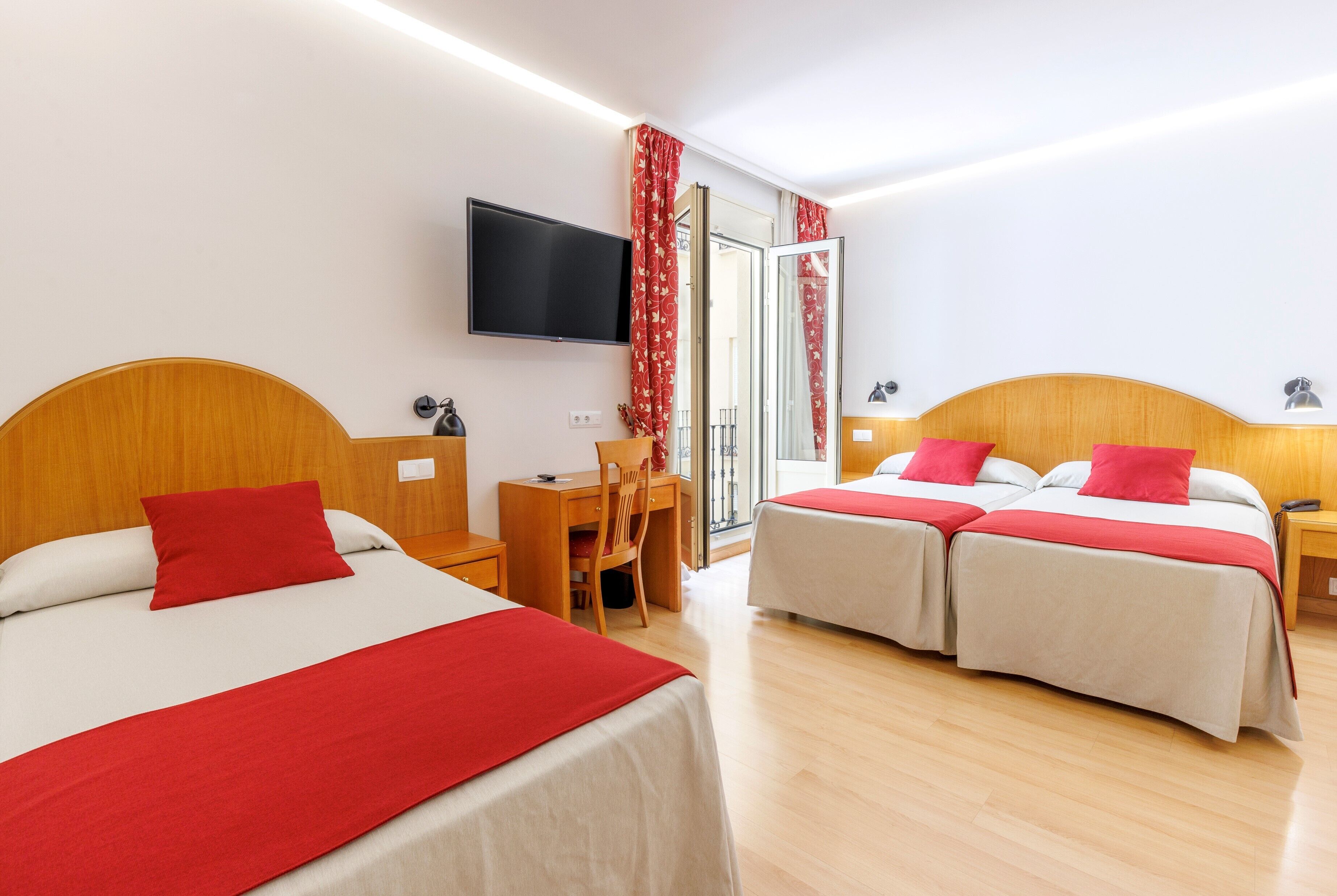 Una habitación de hotel con dos camas, un escritorio, una silla, un televisor y una puerta corrediza de vidrio.