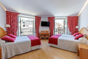 A hotel room with two beds, a TV, a balcony with red curtains, and a wooden floor.