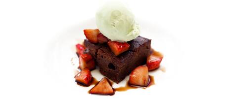 A dessert with a scoop of ice cream on top, surrounded by pieces of fruit and drizzled with syrup.