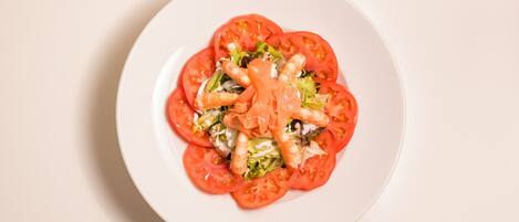 Un plato blanco con una ensalada de tomates, lechuga y camarones.