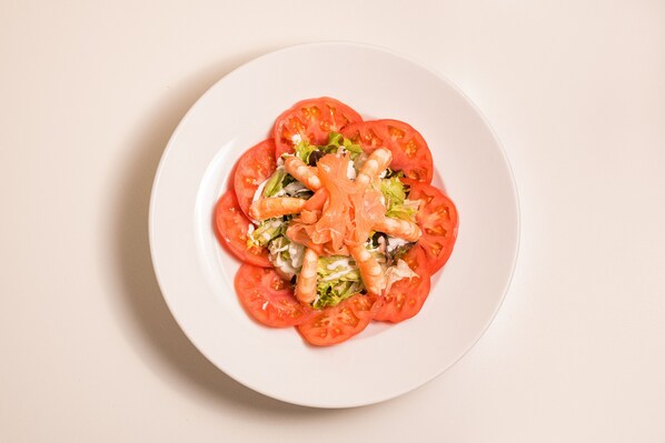 Un plato blanco con una ensalada de tomates, lechuga y camarones.
