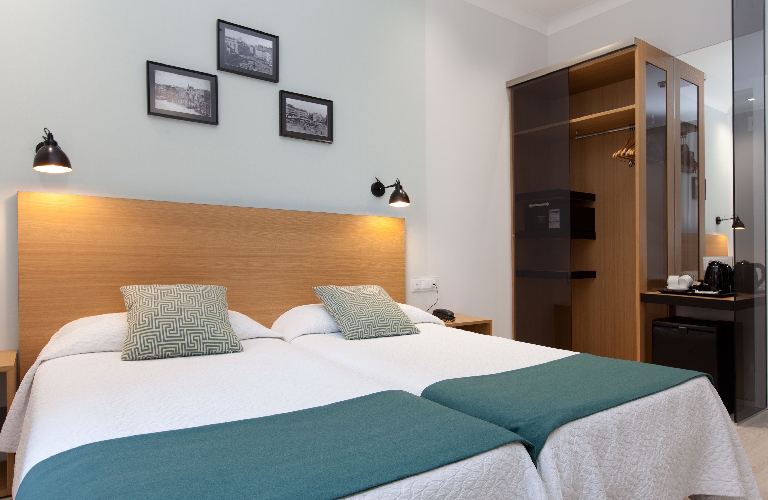 A hotel room with a large bed, two bedside lamps, a wooden headboard, a closet with a mirror, and a small desk with a coffee maker.