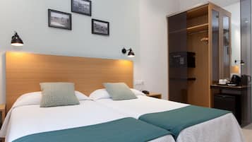 Une chambre d’hôtel avec un grand lit, deux lampes de chevet, une tête de lit en bois, une armoire avec un miroir et un petit bureau avec une machine à café.