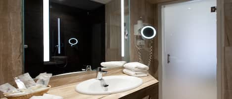 A modern bathroom with a large mirror, a sink, and a hairdryer. There are towels and toiletries on the counter.