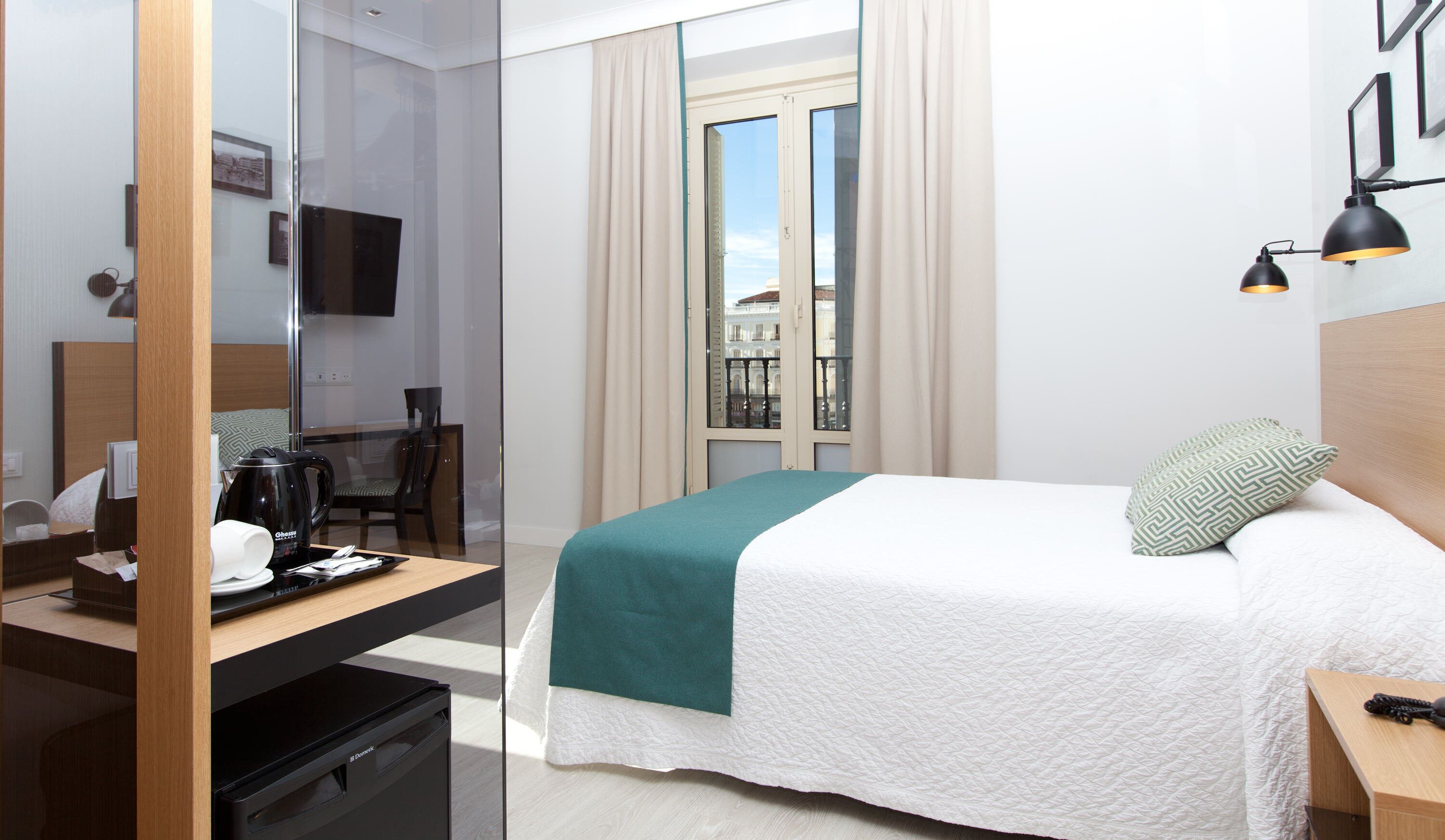Una habitación de hotel con una cama, un escritorio con cafetera, una silla, un televisor y una ventana con cortinas.