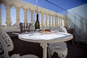 Un tavolo rotondo con una bottiglia di champagne, un bicchiere e una fetta di torta su un balcone con sedie bianche e una ringhiera.