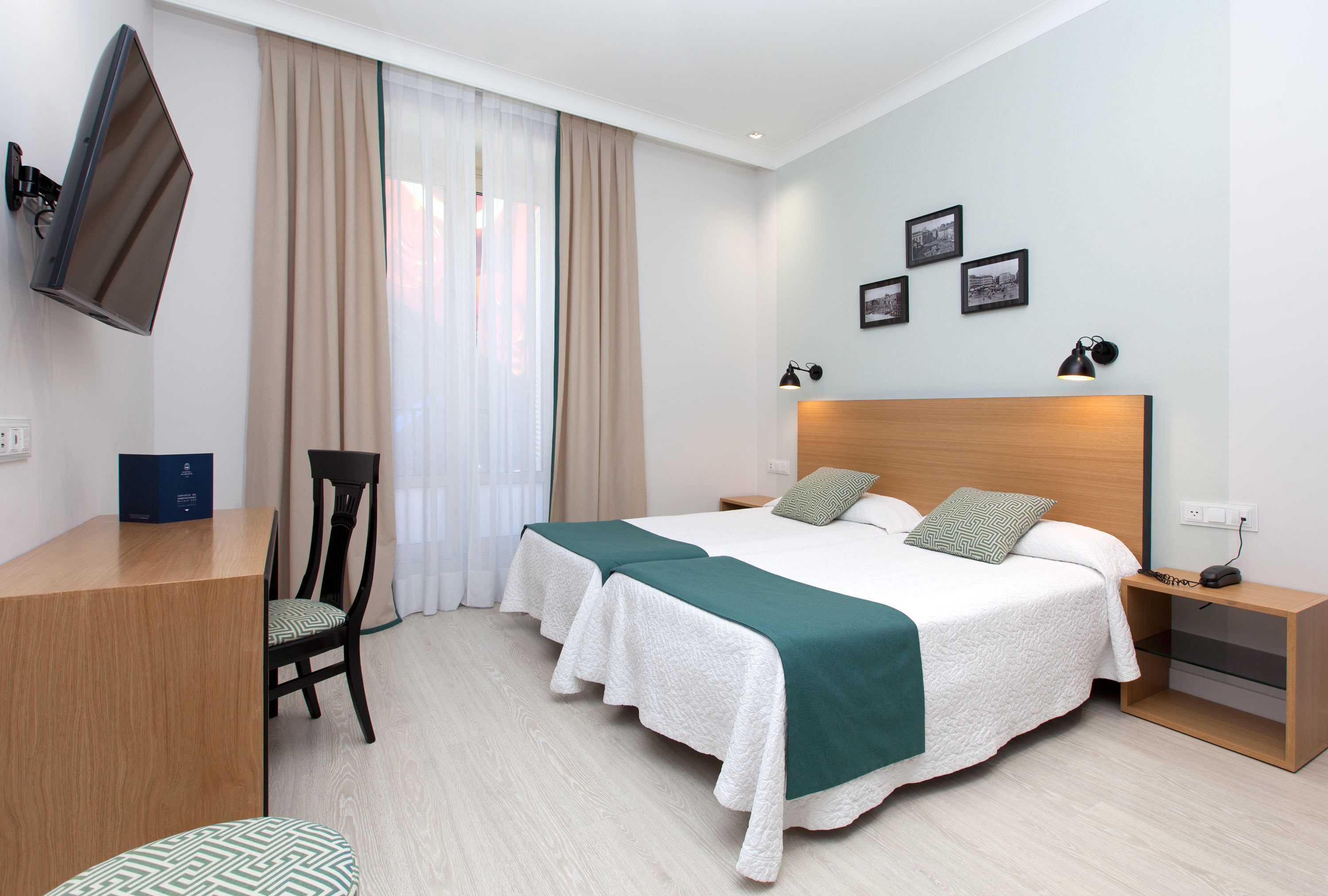 Una habitación de hotel con cama, escritorio, silla, televisor y mesita de noche.