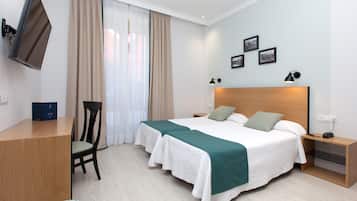 Una habitación de hotel con cama, escritorio, silla, televisor y mesita de noche.