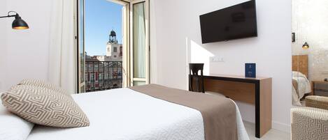 A hotel room with a bed, a desk, a TV, and a view of a cityscape.