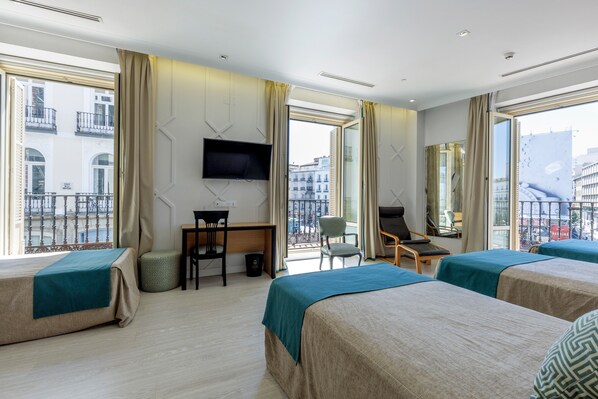 A hotel room with two beds, a desk, a chair, a TV, and large windows with a city view. - Hotel Europa (Madrid)