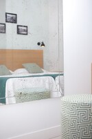 A bedroom with a bed, a bedside table, and a mirror reflecting the room.