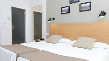 A double bed with two pillows, a wooden headboard, and a beige throw blanket. There are two wall-mounted lamps and three framed pictures on the wall.