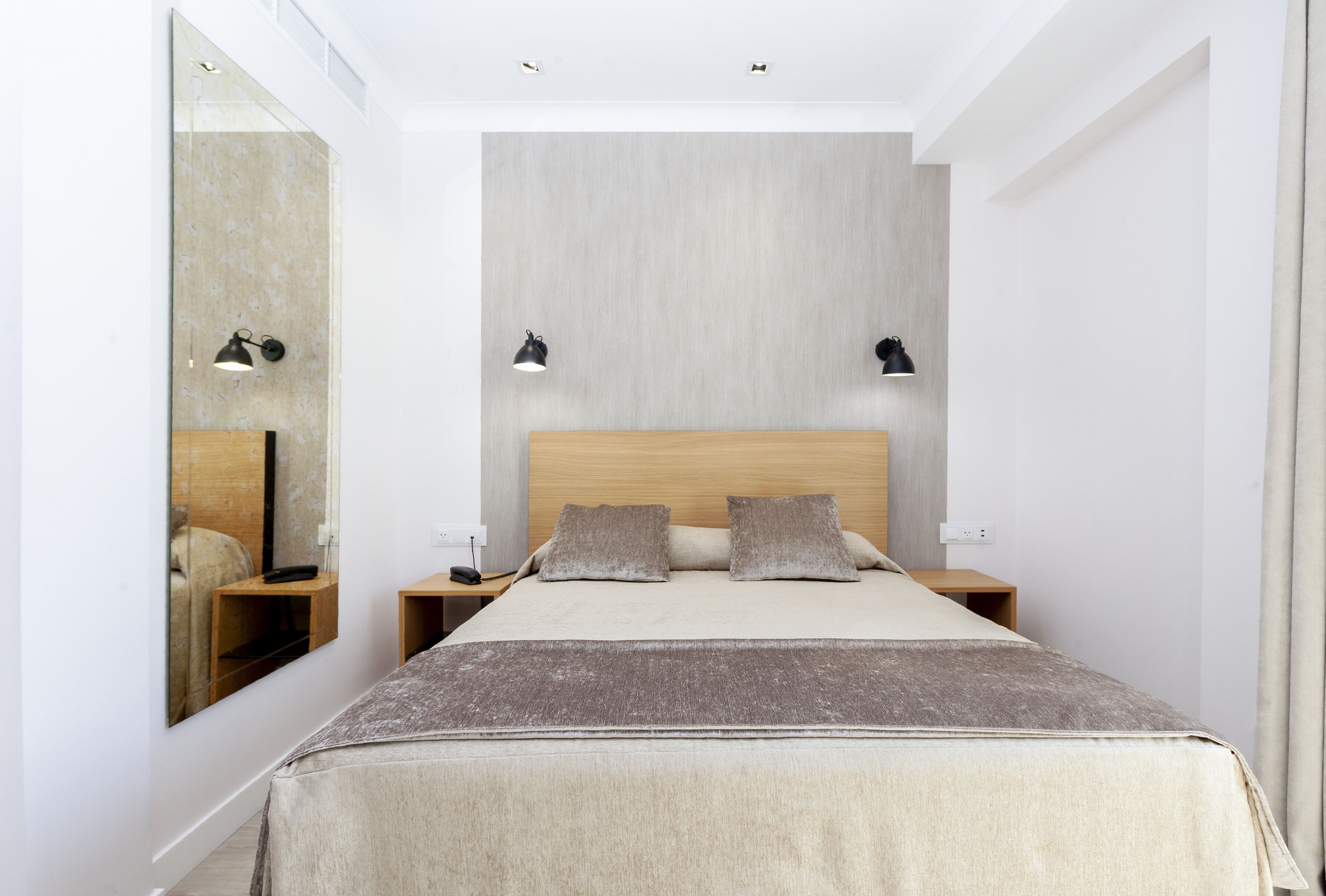 Un dormitorio moderno con una cama grande, dos mesitas de noche, un espejo y dos lámparas de pared.