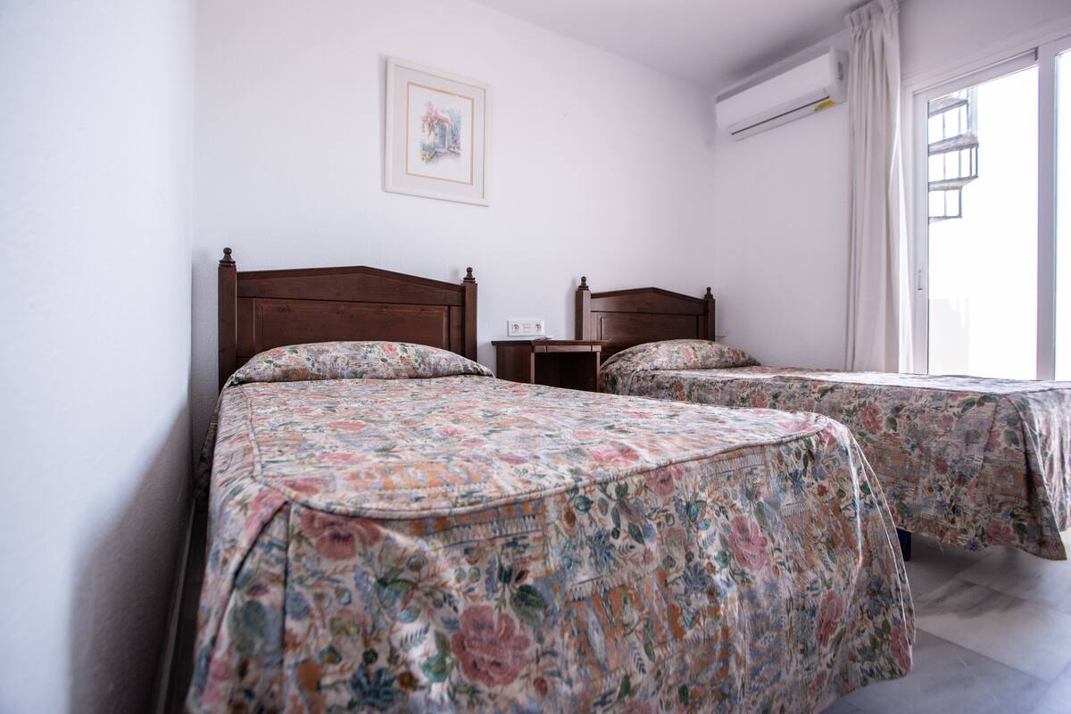 Habitación de hotel con dos camas, una mesita de noche, un equipo de aire acondicionado y una ventana con cortinas.