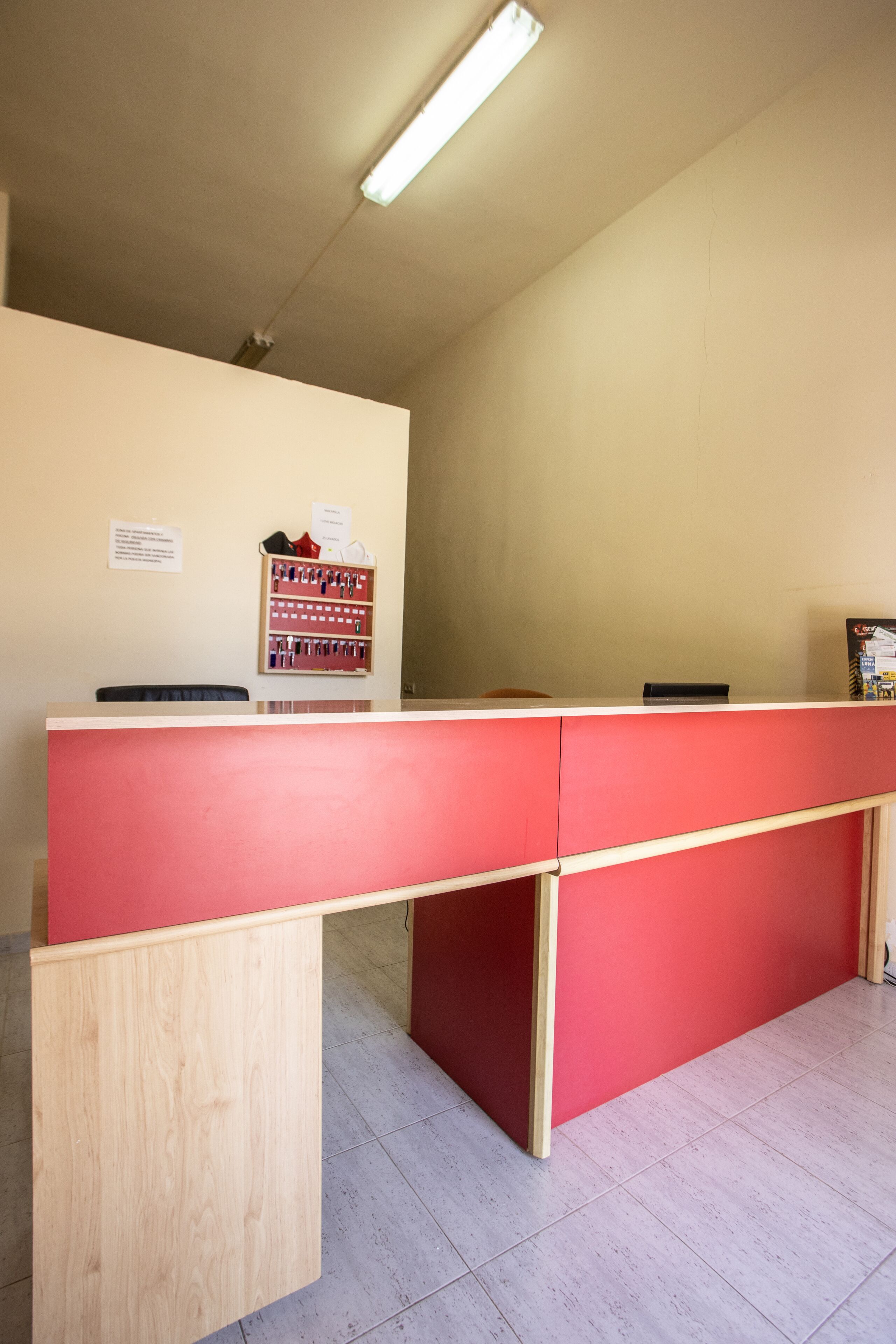 Een receptiebalie met een rode toonbank en een houten bureau links. Achter de balie hangt een prikbord met mededelingen.